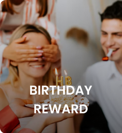 A group celebrating a birthday with a cake, candles, and one person playfully covering another's eyes